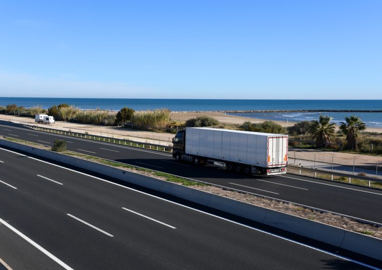 Image of a semi truck on freeway near the beach. Driving by someone hired by CDL staffing in Ventura